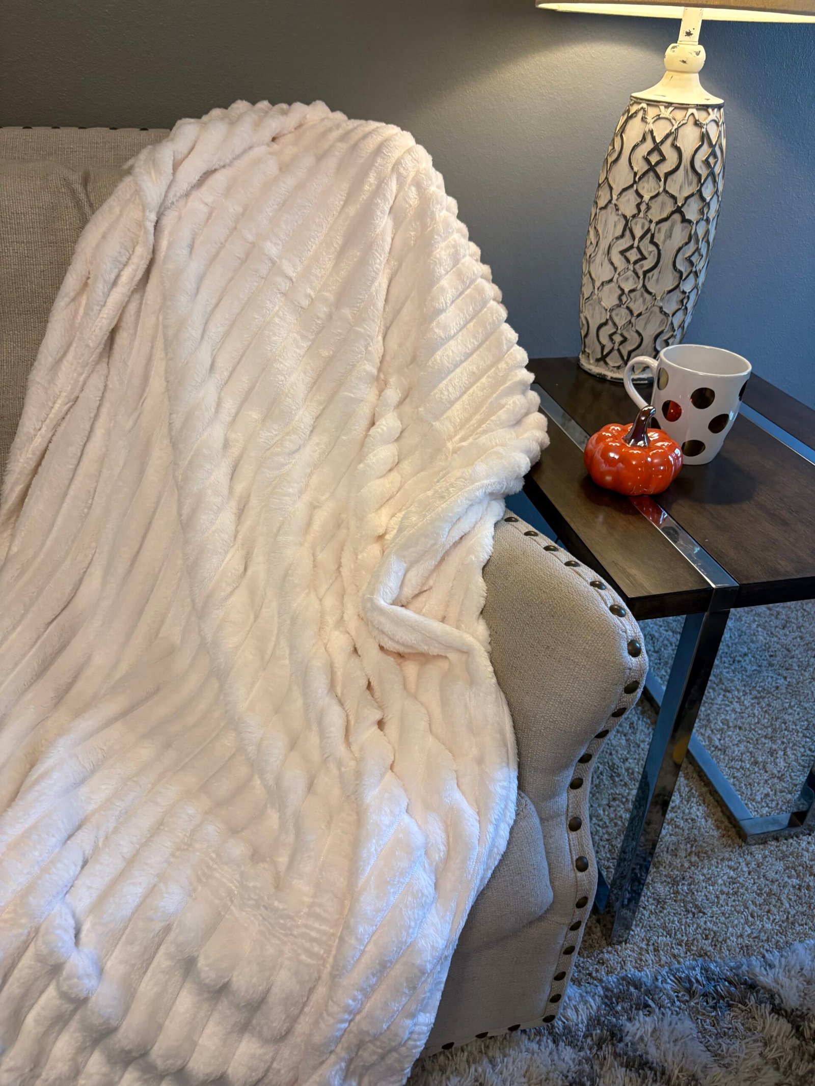white ribbed blanket draped over couch with pumpkin, lamp, and coffee cup.